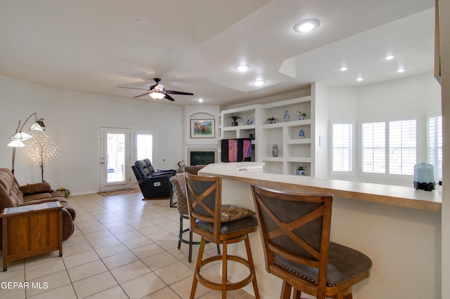 kitchen featuring light tile patterned floors, ceiling fan, a glass covered fireplace, a kitchen breakfast bar, and open floor plan