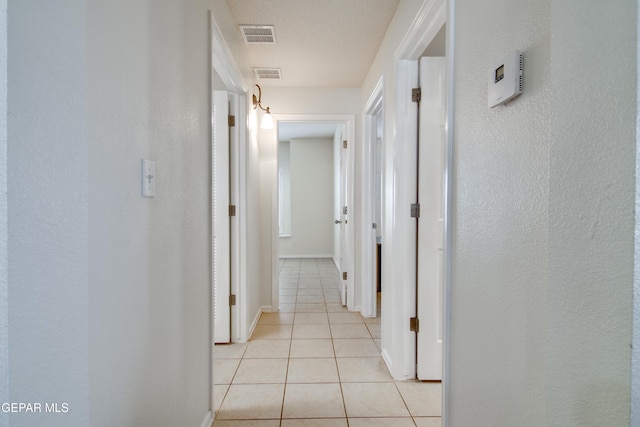 hall featuring light tile patterned floors, visible vents, and baseboards