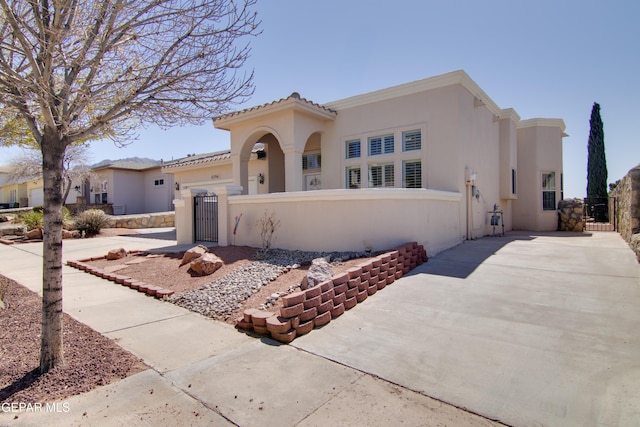 mediterranean / spanish-style home with a fenced front yard, stucco siding, driveway, and a gate