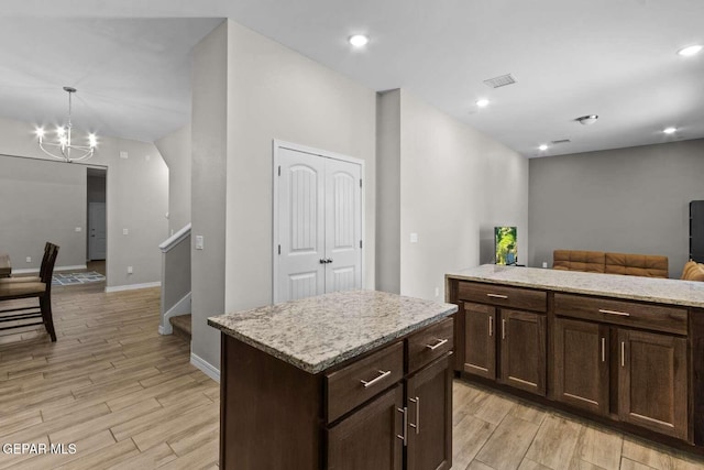 kitchen featuring a kitchen island, light stone countertops, open floor plan, light wood-style flooring, and an inviting chandelier