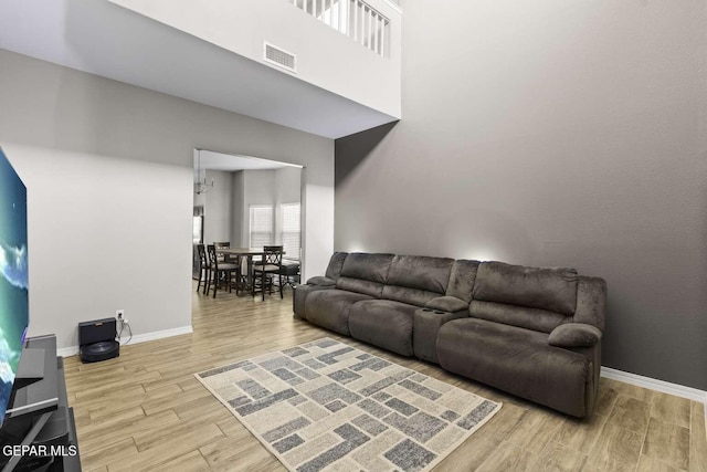 living room with visible vents, baseboards, a high ceiling, an inviting chandelier, and wood finished floors