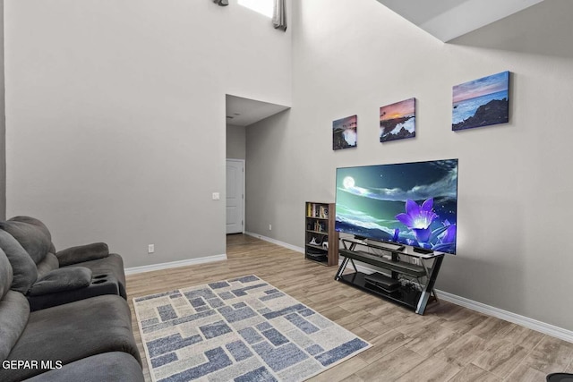 living area with a high ceiling, baseboards, and wood finished floors