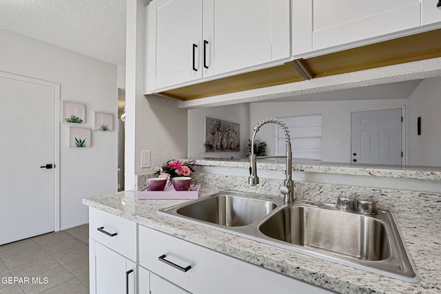 kitchen featuring a sink, a textured ceiling, light tile patterned floors, and white cabinetry