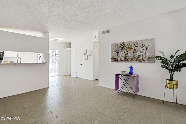 unfurnished living room with tile patterned flooring, visible vents, a textured ceiling, and a sink