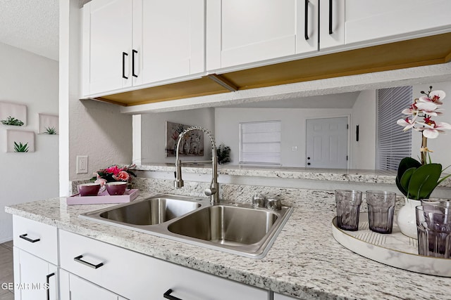 kitchen with white cabinets, light stone countertops, and a sink