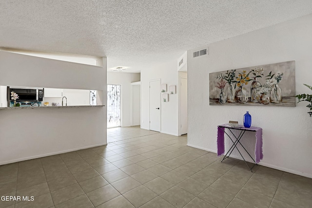 unfurnished living room with tile patterned floors, visible vents, a textured ceiling, and a textured wall