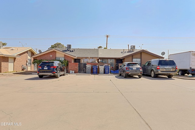 view of front facade with central air condition unit, brick siding, and uncovered parking