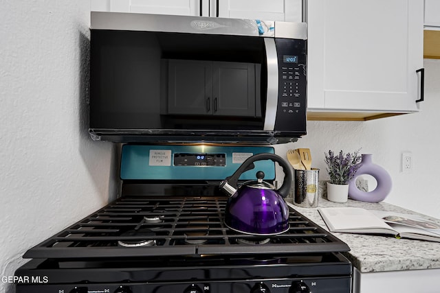 room details with stainless steel microwave, light stone counters, range with gas stovetop, a textured wall, and white cabinets