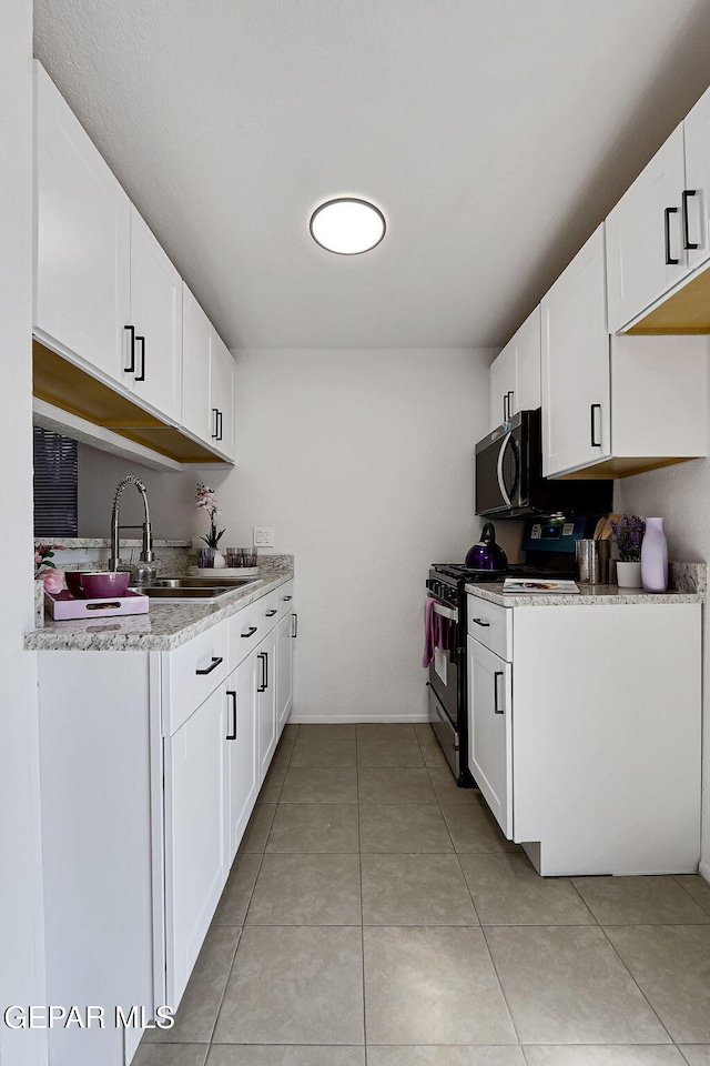 kitchen with a sink, appliances with stainless steel finishes, light tile patterned flooring, and white cabinets