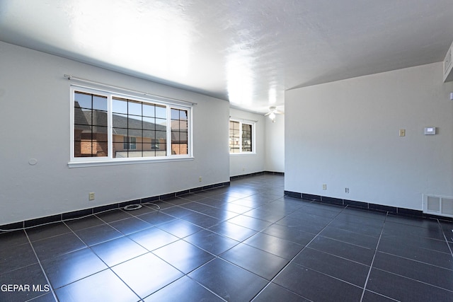 empty room with visible vents, baseboards, dark tile patterned floors, and a ceiling fan