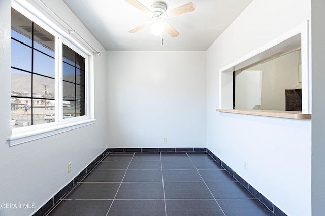 empty room with baseboards, dark tile patterned flooring, and a ceiling fan