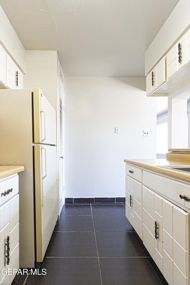 kitchen featuring light countertops, white cabinets, baseboards, and freestanding refrigerator