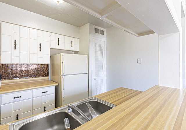 kitchen featuring visible vents, freestanding refrigerator, a sink, white cabinetry, and backsplash