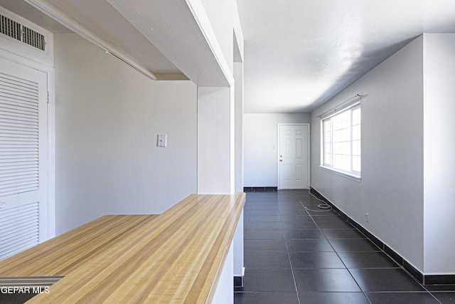 hall featuring dark tile patterned floors, baseboards, and visible vents