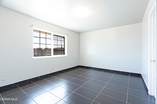 unfurnished room featuring baseboards and dark tile patterned flooring