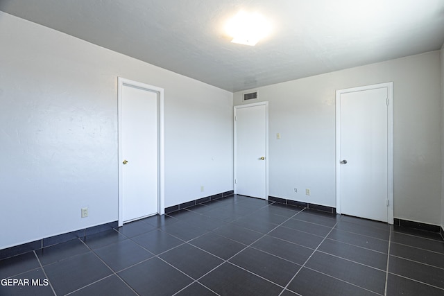 unfurnished bedroom with visible vents, baseboards, and dark tile patterned floors