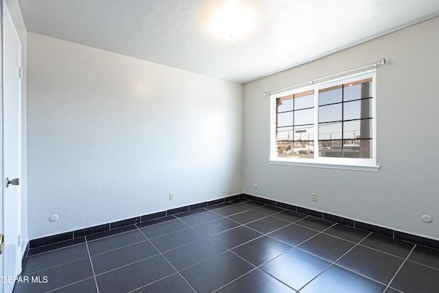 empty room featuring dark tile patterned floors and baseboards