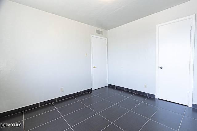 empty room featuring dark tile patterned floors, visible vents, and baseboards