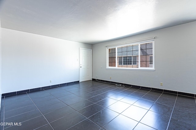 spare room featuring dark tile patterned floors and baseboards