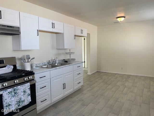 kitchen featuring stainless steel range with gas cooktop, under cabinet range hood, light wood-type flooring, light countertops, and a sink