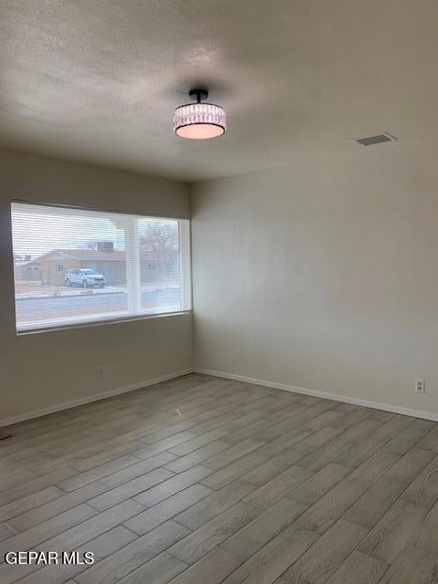 unfurnished room with visible vents, wood finished floors, and baseboards