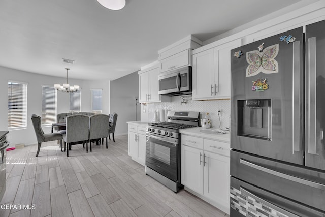 kitchen featuring stainless steel appliances, light countertops, white cabinets, backsplash, and a chandelier