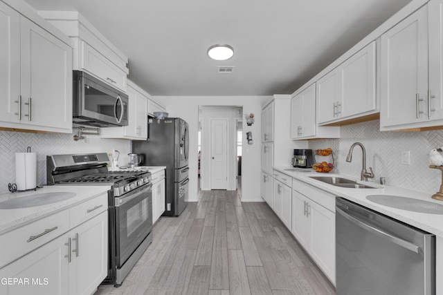 kitchen with light wood finished floors, white cabinets, stainless steel appliances, and a sink