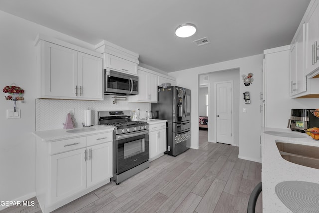 kitchen with tasteful backsplash, visible vents, light wood-style flooring, stainless steel appliances, and white cabinetry