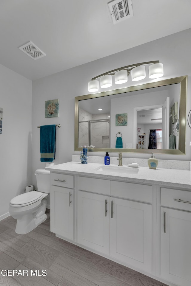 bathroom featuring visible vents, a stall shower, toilet, and vanity