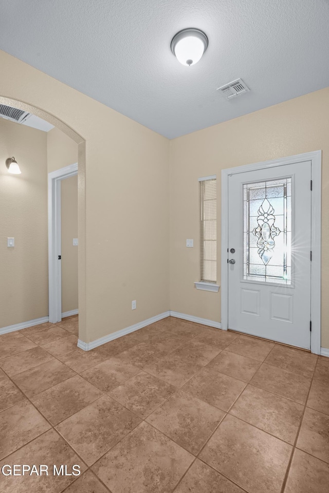 entrance foyer with baseboards, visible vents, arched walkways, and a textured ceiling