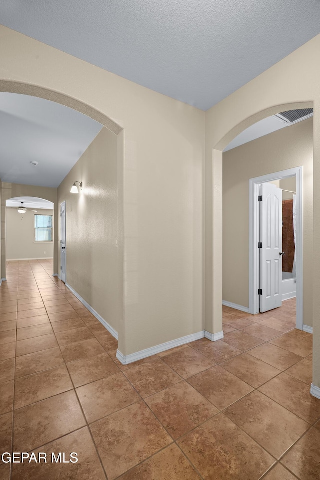 hall featuring arched walkways, tile patterned flooring, visible vents, and baseboards