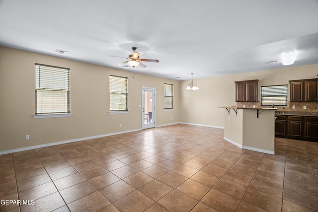 unfurnished living room featuring tile patterned floors, visible vents, ceiling fan with notable chandelier, and baseboards