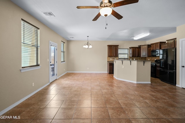 kitchen with visible vents, a breakfast bar, black appliances, ceiling fan with notable chandelier, and tasteful backsplash