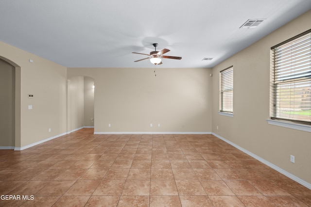 spare room featuring plenty of natural light, visible vents, arched walkways, and ceiling fan