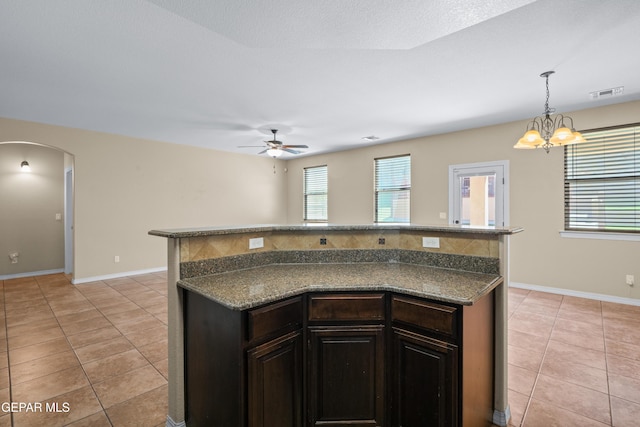 kitchen featuring light tile patterned floors, ceiling fan with notable chandelier, arched walkways, and dark countertops