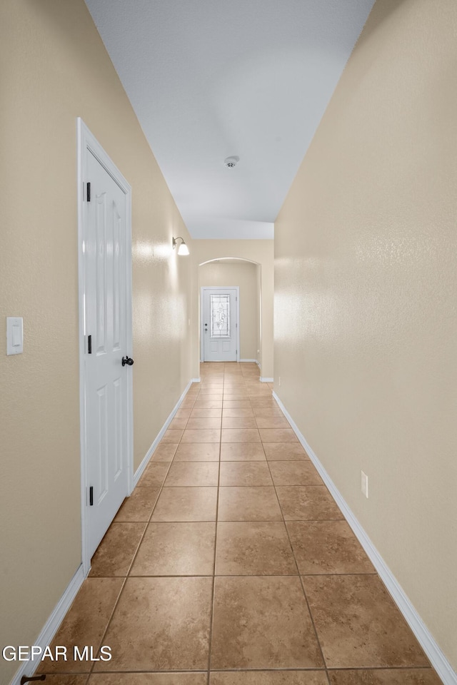 corridor with arched walkways, baseboards, and light tile patterned flooring