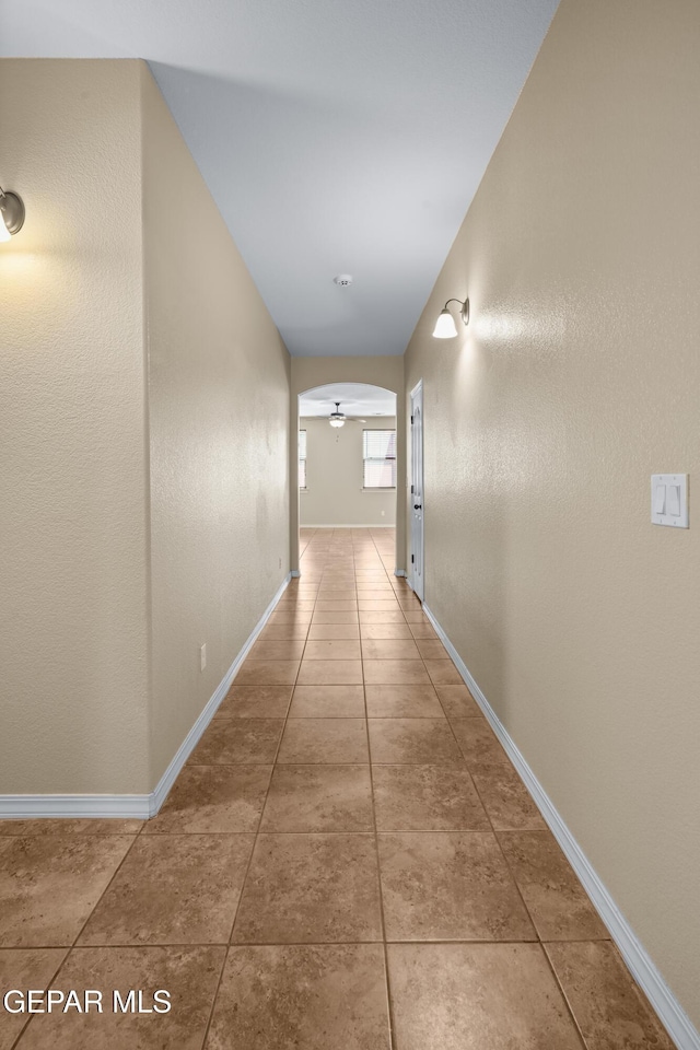 hall with arched walkways, tile patterned flooring, and baseboards