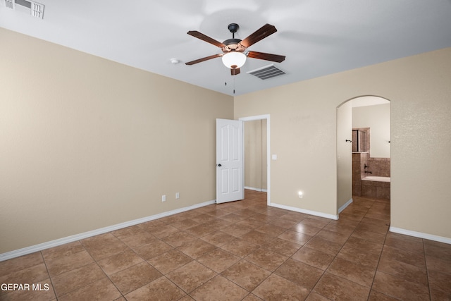 tiled spare room featuring arched walkways, visible vents, baseboards, and a ceiling fan