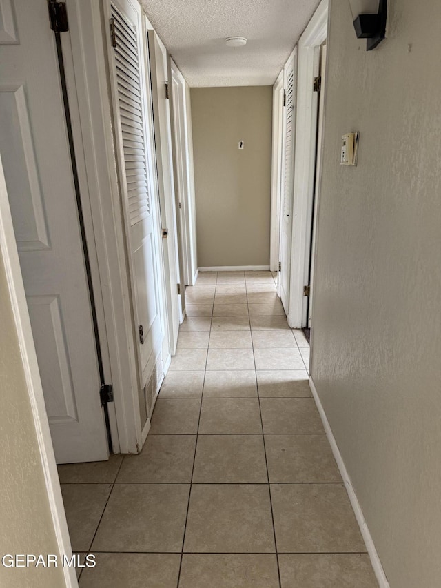 hallway featuring light tile patterned floors, a textured ceiling, and baseboards