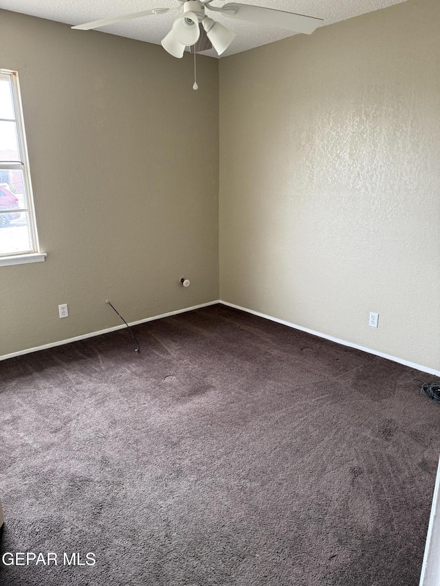 empty room with dark colored carpet, baseboards, a textured ceiling, and ceiling fan