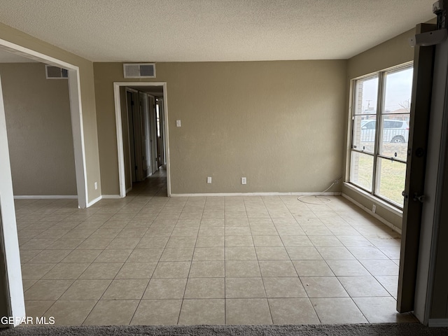 empty room featuring light tile patterned flooring, baseboards, visible vents, and a textured ceiling