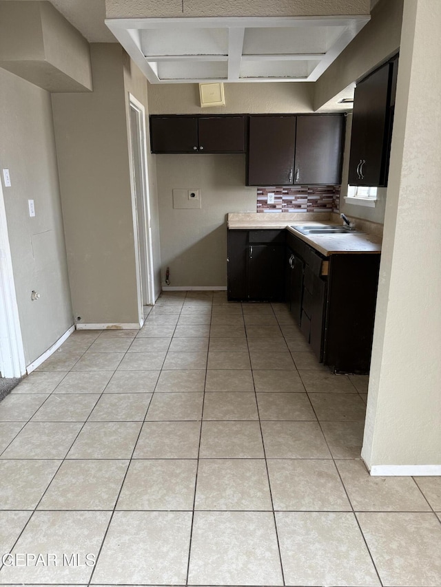 kitchen featuring a sink, backsplash, light countertops, light tile patterned floors, and baseboards