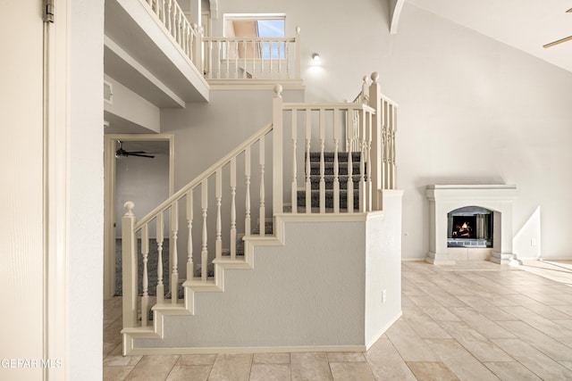 stairway featuring a warm lit fireplace, ceiling fan, and a towering ceiling