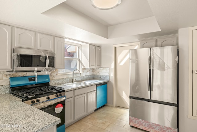 kitchen with a tray ceiling, a sink, light countertops, appliances with stainless steel finishes, and backsplash