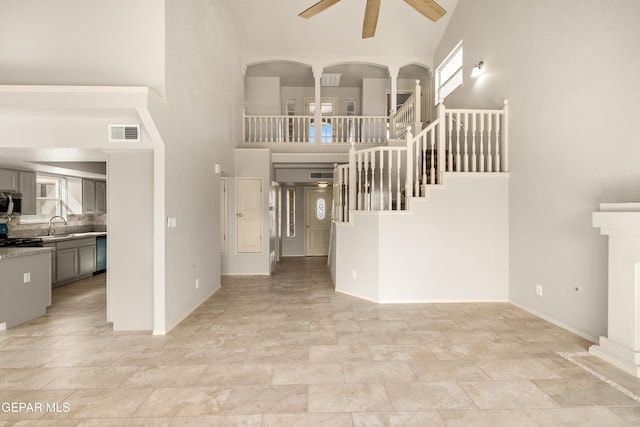 living area with visible vents, a towering ceiling, baseboards, ceiling fan, and stairs