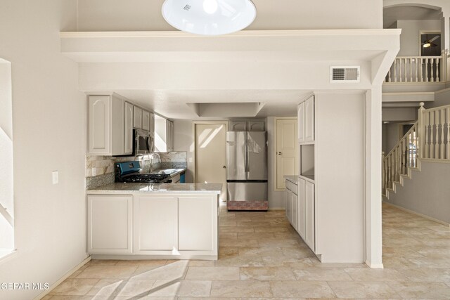 kitchen featuring baseboards, visible vents, a peninsula, decorative backsplash, and appliances with stainless steel finishes