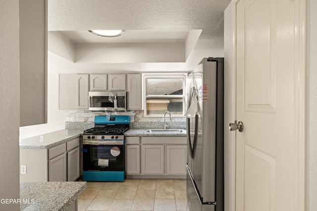 kitchen featuring tasteful backsplash, light stone countertops, appliances with stainless steel finishes, a textured ceiling, and a sink