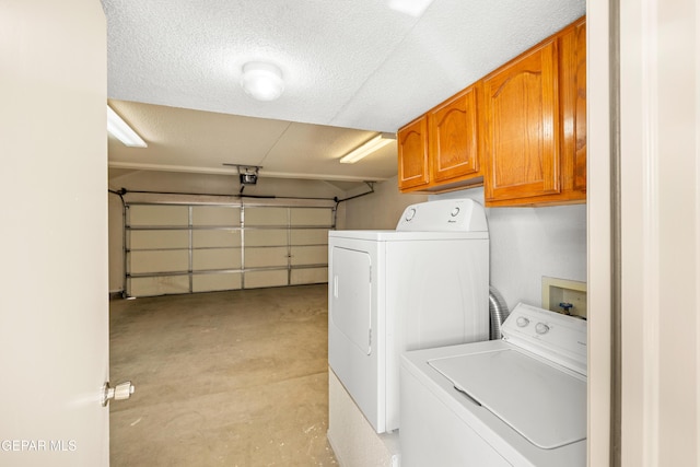 washroom featuring washing machine and clothes dryer, cabinet space, and a textured ceiling