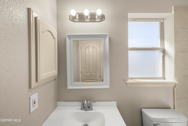 bathroom featuring a sink, toilet, and a textured wall