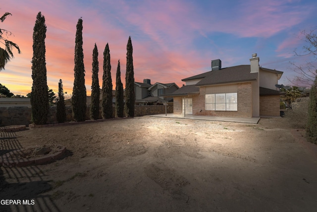 back of property at dusk with brick siding and a chimney